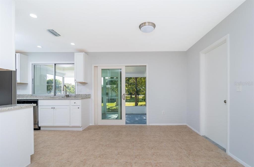 A kitchen and dining area with white cabinets, granite countertops, tile flooring, and a sliding door — 533 E CHARLOTTE AVENUE, PUNTA GORDA, FL
