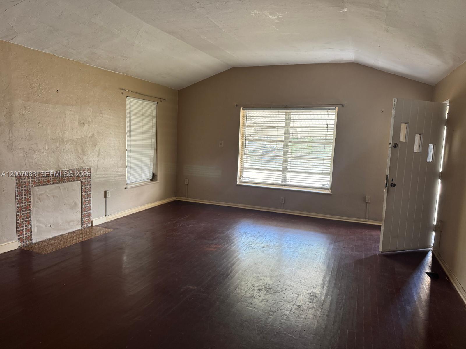 An empty living room features dark wood floors, a tiled fireplace, and a white door — 1812 Fillmore St, Hollywood FL 33020, HOLLYWOOD, FL