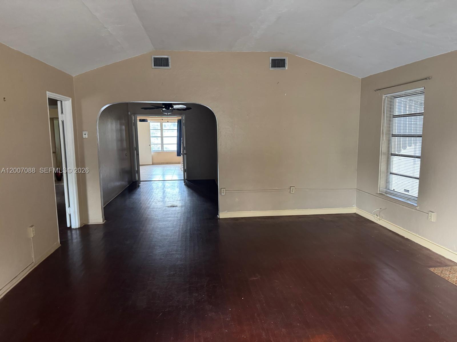 An empty room with dark wood floors, beige walls, and an arched doorway — 1812 Fillmore St, Hollywood FL 33020, HOLLYWOOD, FL