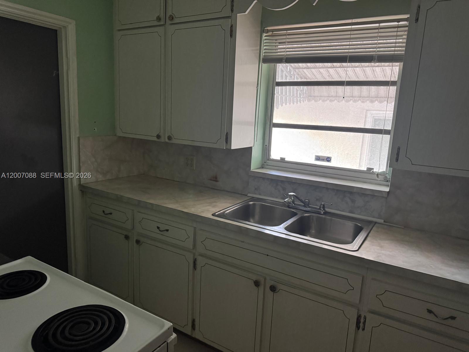 A kitchen features white cabinets, a double-basin stainless steel sink, and a window with blinds — 1812 Fillmore St, Hollywood FL 33020, HOLLYWOOD, FL