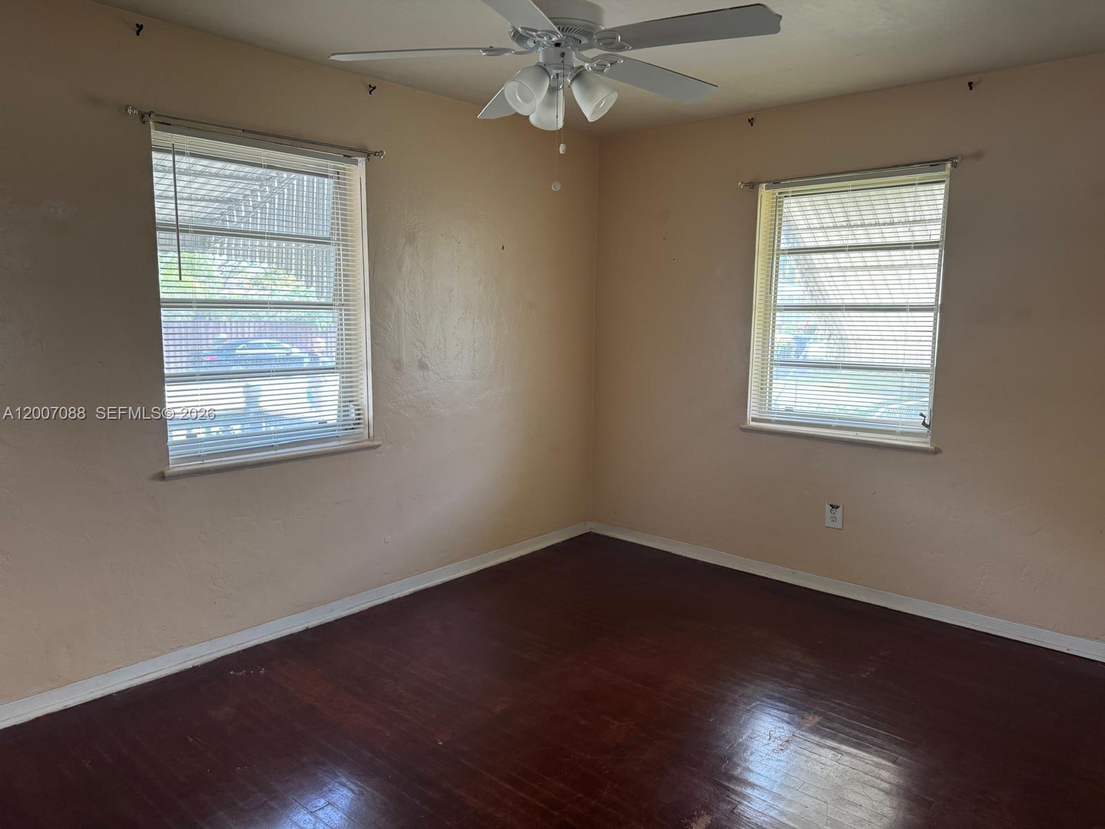 An empty room features dark wood floors, beige walls, two windows, and a ceiling fan — 1812 Fillmore St, Hollywood FL 33020, HOLLYWOOD, FL