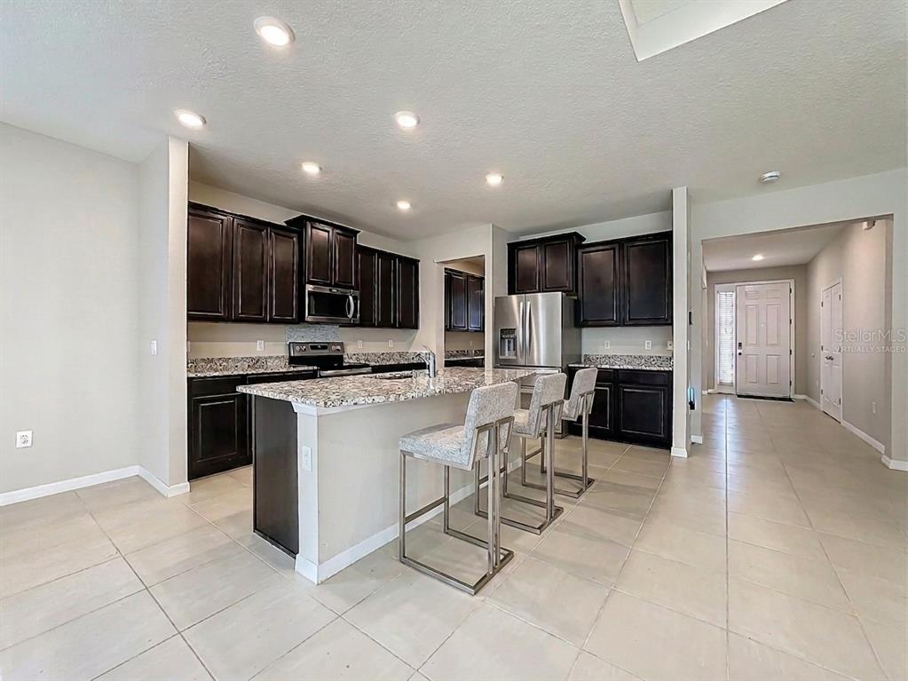A kitchen features dark wood cabinets, granite countertops, a center island, and tile flooring — 13071 BROOKSIDE MOSS DRIVE, RIVERVIEW, FL
