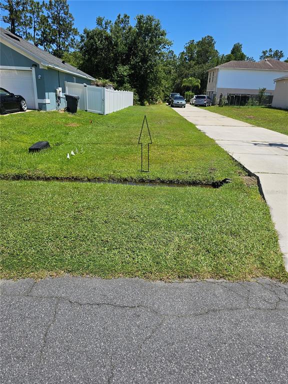 A grassy residential lot sits between a house with a white fence and a driveway — 0 ROBIN LANE, POINCIANA, FL