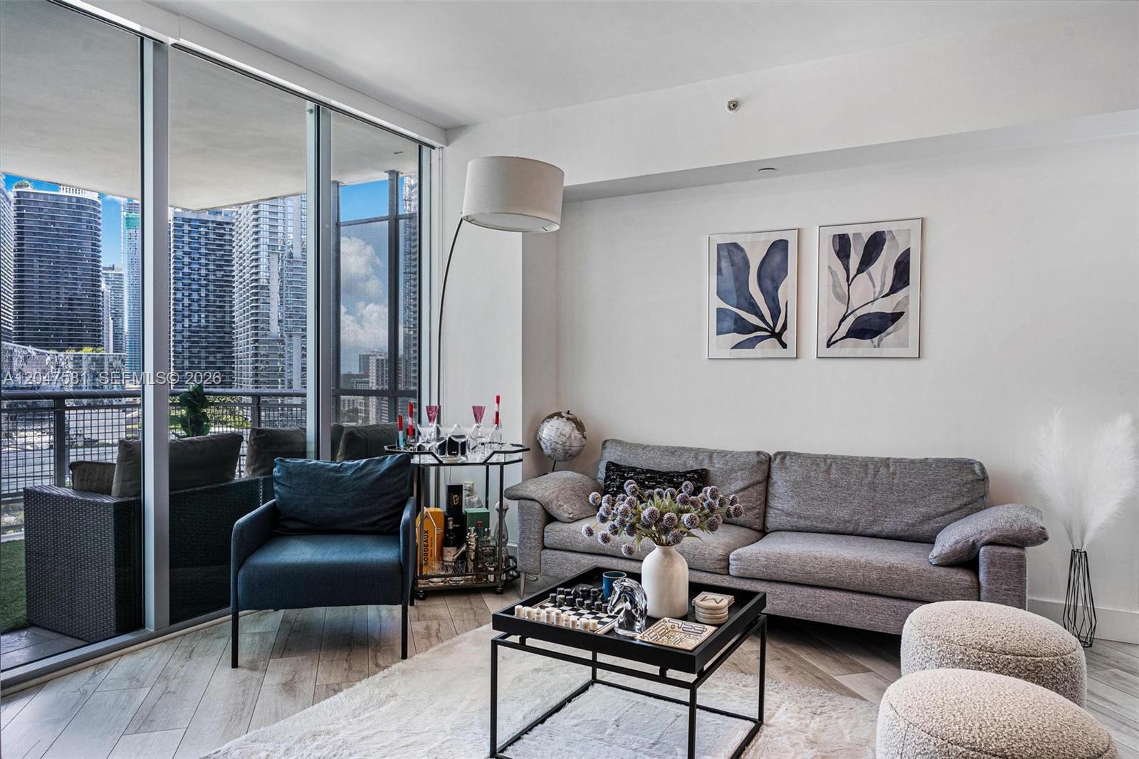 A modern living room features a grey sofa, blue armchair, and a city balcony view — 350 S Miami Ave # 2108, Miami FL 33130, MIAMI, FL