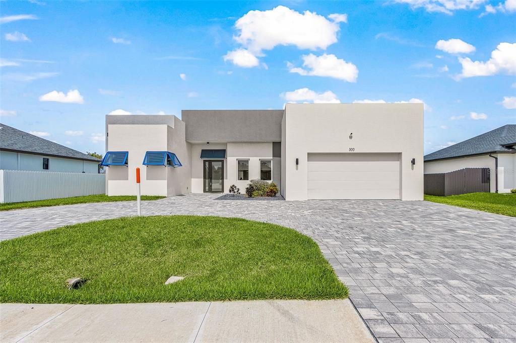 A modern, single-story house with a paved driveway, two-car garage, and blue window awnings — 300 CHIQUITA BOULEVARD N, CAPE CORAL, FL