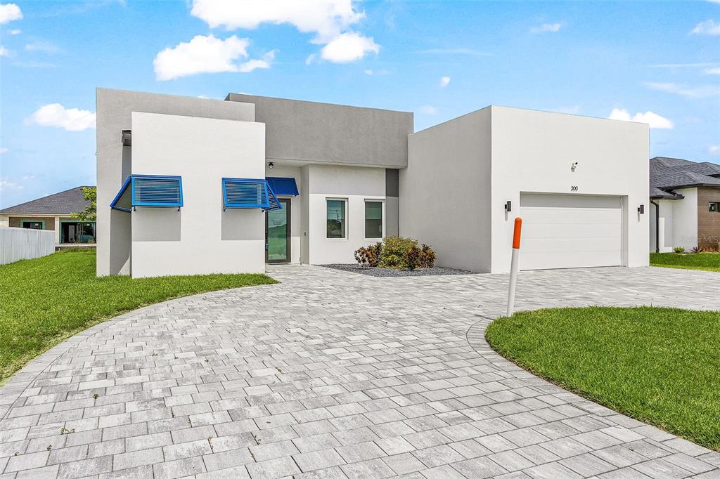 A modern, single-story house with a paved driveway, white stucco exterior, and blue window awnings — 300 CHIQUITA BOULEVARD N, CAPE CORAL, FL