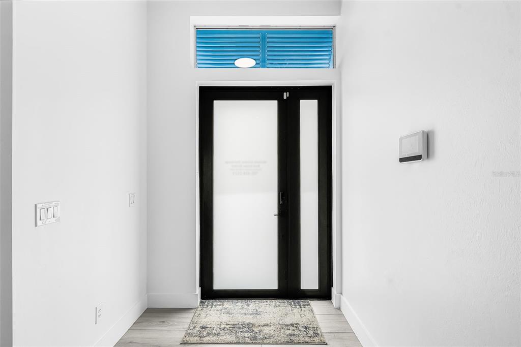 A modern entryway features a black-framed glass door, a transom window, and white walls — 300 CHIQUITA BOULEVARD N, CAPE CORAL, FL