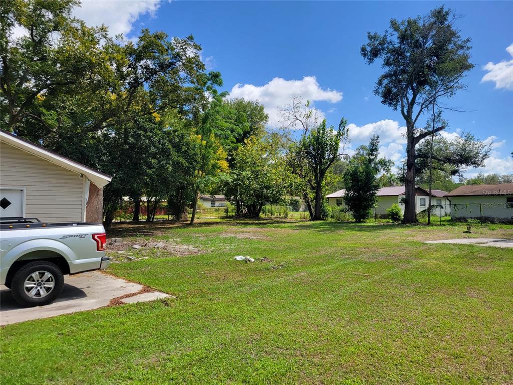 A grassy backyard features mature trees, a concrete driveway, and a partial view of a house — 38606 CALUMET AVENUE, ZEPHYRHILLS, FL