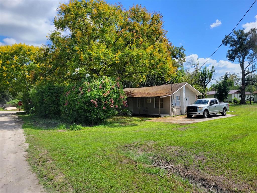 A single-story house with beige siding sits on a grassy lot near a large tree — 38606 CALUMET AVENUE, ZEPHYRHILLS, FL