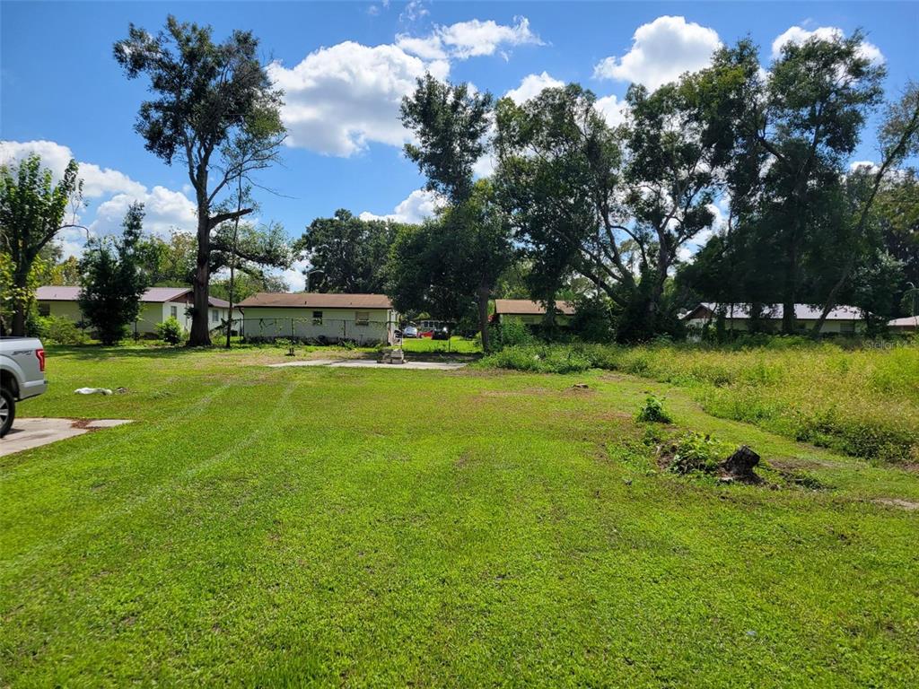 A large, grassy vacant lot features a concrete pad and mature trees under a blue sky — 38606 CALUMET AVENUE, ZEPHYRHILLS, FL