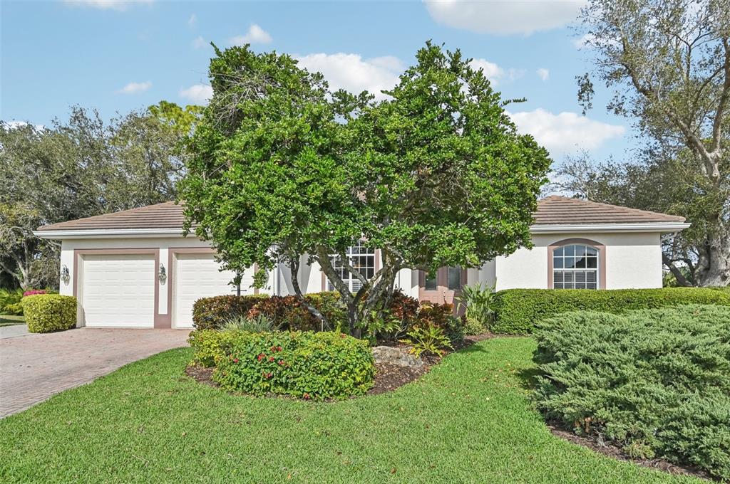 A single-story house with a two-car garage, a large central tree, and landscaped front yard — 514 SUMMERFIELD WAY, VENICE, FL