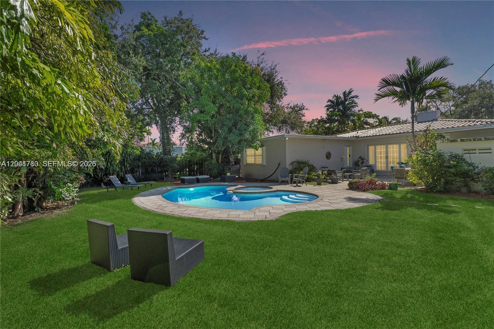 A backyard features a swimming pool, stone patio, green lawn, and a single-story house — 1875 Alamanda Dr # 1875, North Miami FL 33181, NORTH MIAMI, FL