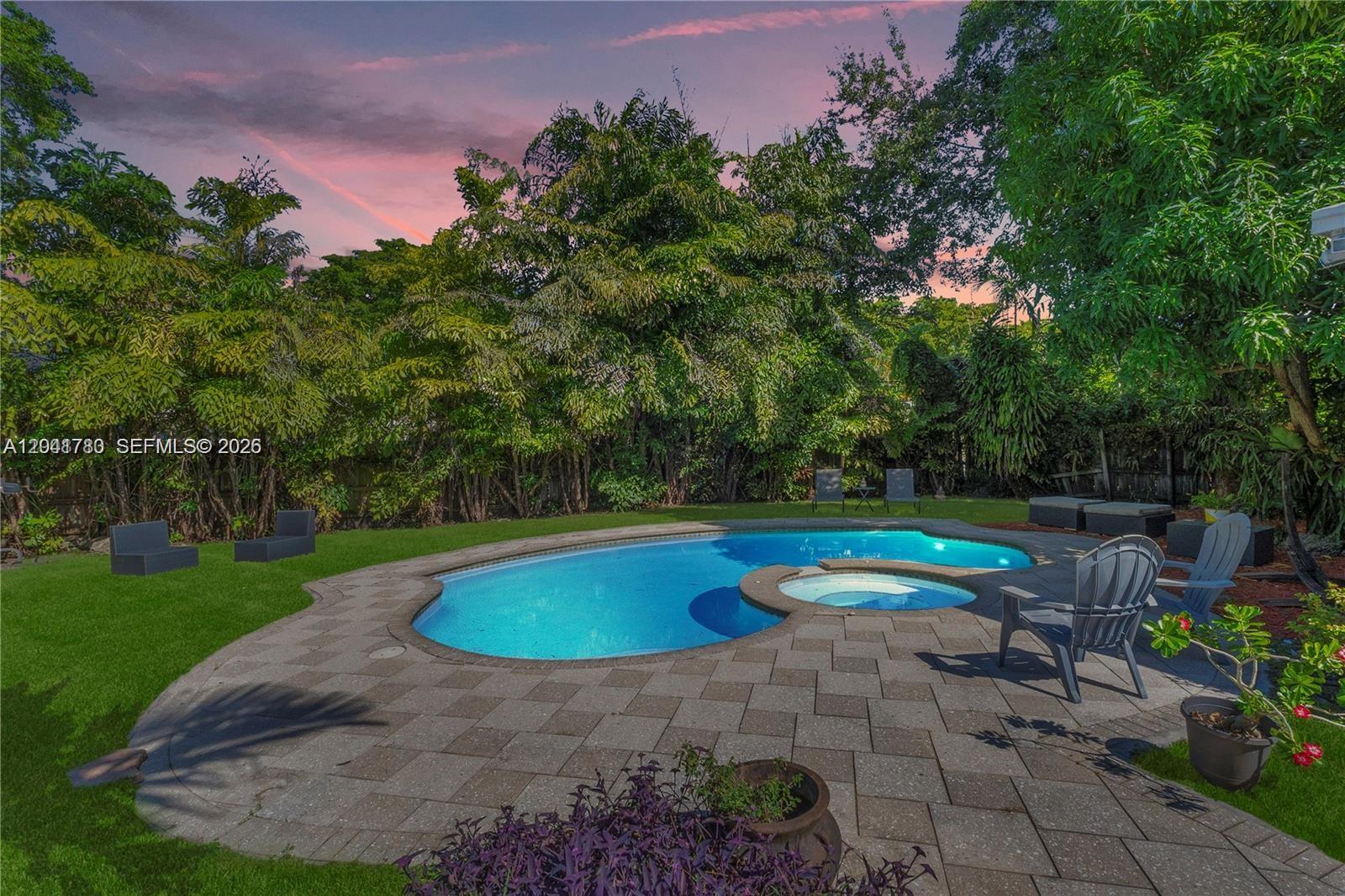 A backyard features a swimming pool with an integrated spa and a stone paver patio — 1875 Alamanda Dr # 1875, North Miami FL 33181, NORTH MIAMI, FL