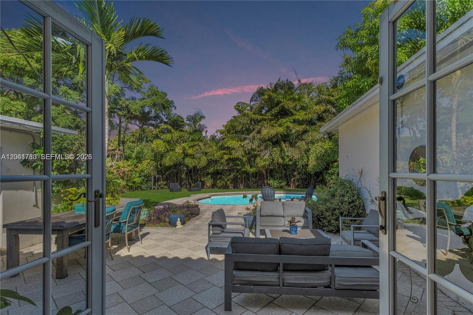 A patio with outdoor furniture and a swimming pool is viewed through open French doors — 1875 Alamanda Dr # 1875, North Miami FL 33181, NORTH MIAMI, FL