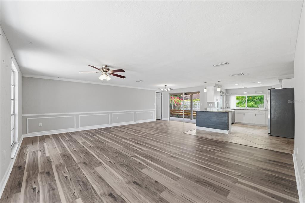 An open-concept living room with wood-look flooring, wainscoting, and an adjacent kitchen with a peninsula — 4018 CASHMERE DRIVE, NEW PORT RICHEY, FL