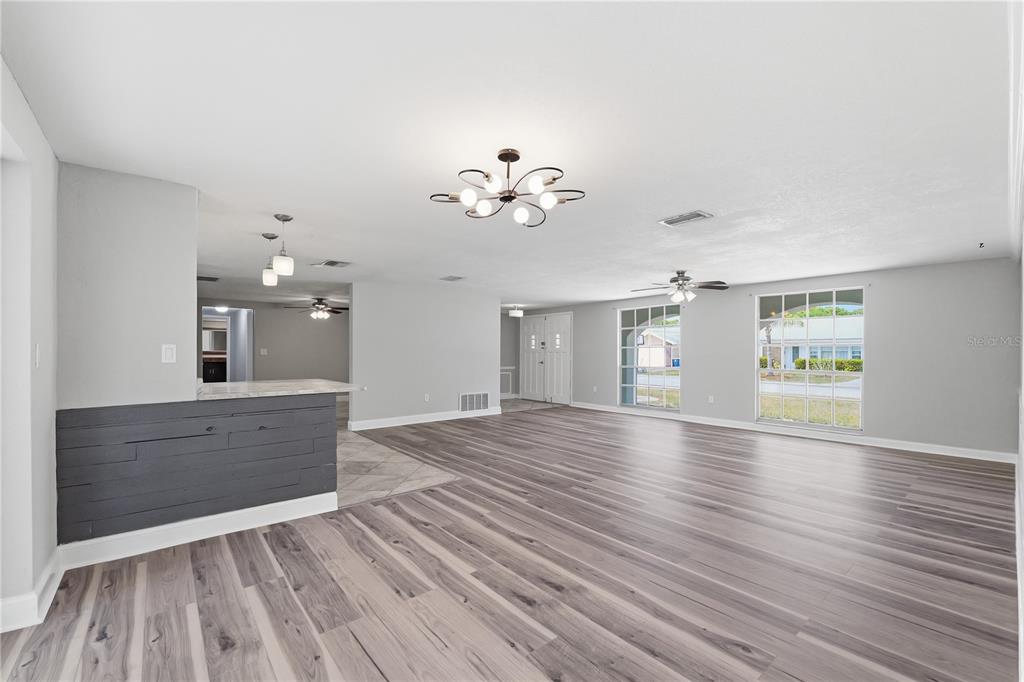 A spacious living room features light gray walls, wood-look flooring, and a dark shiplap breakfast bar — 4018 CASHMERE DRIVE, NEW PORT RICHEY, FL