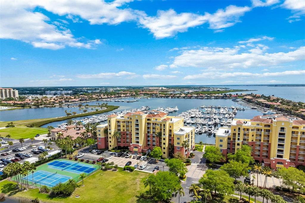 An aerial view shows a large waterfront apartment complex with a marina and tennis courts — 606 RIVIERA DUNES WAY UNIT 601, PALMETTO, FL