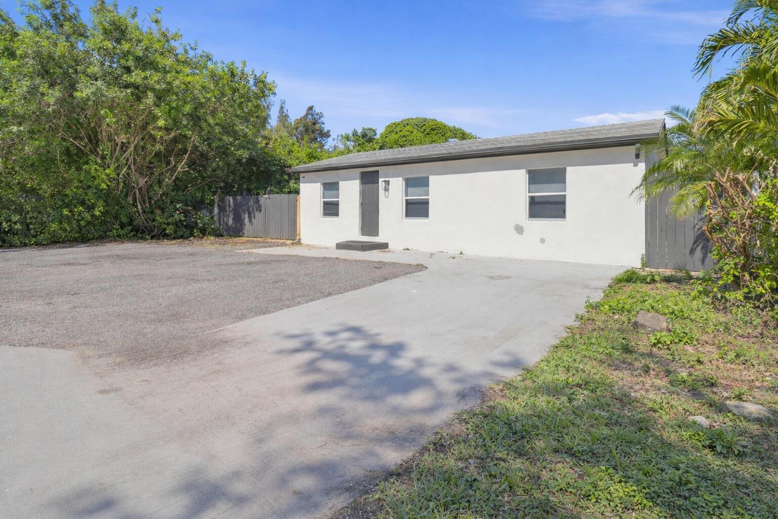 A single-story white house with a gray roof, a concrete driveway, and a gravel area — 1152 Sunset Road, West Palm Beach FL 33406, WEST PALM BEACH, FL