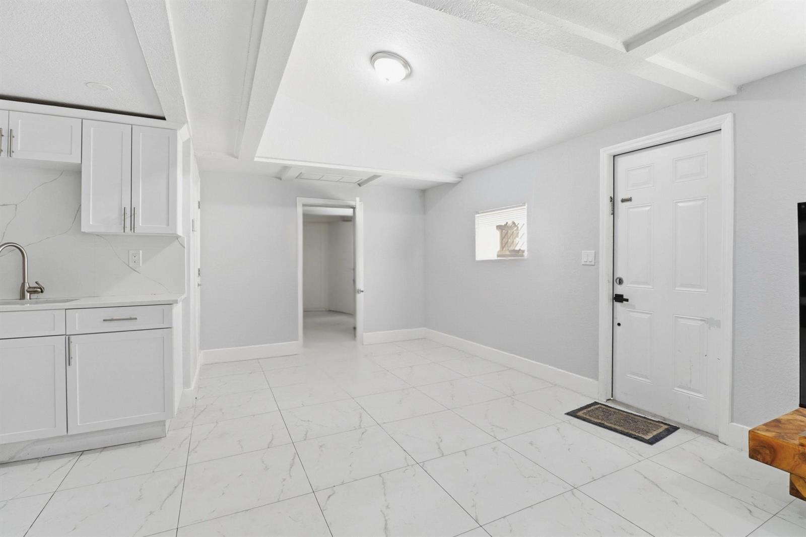 A kitchen area with white cabinets and marble-look tile flooring leads to an interior doorway — 1152 Sunset Road, West Palm Beach FL 33406, WEST PALM BEACH, FL