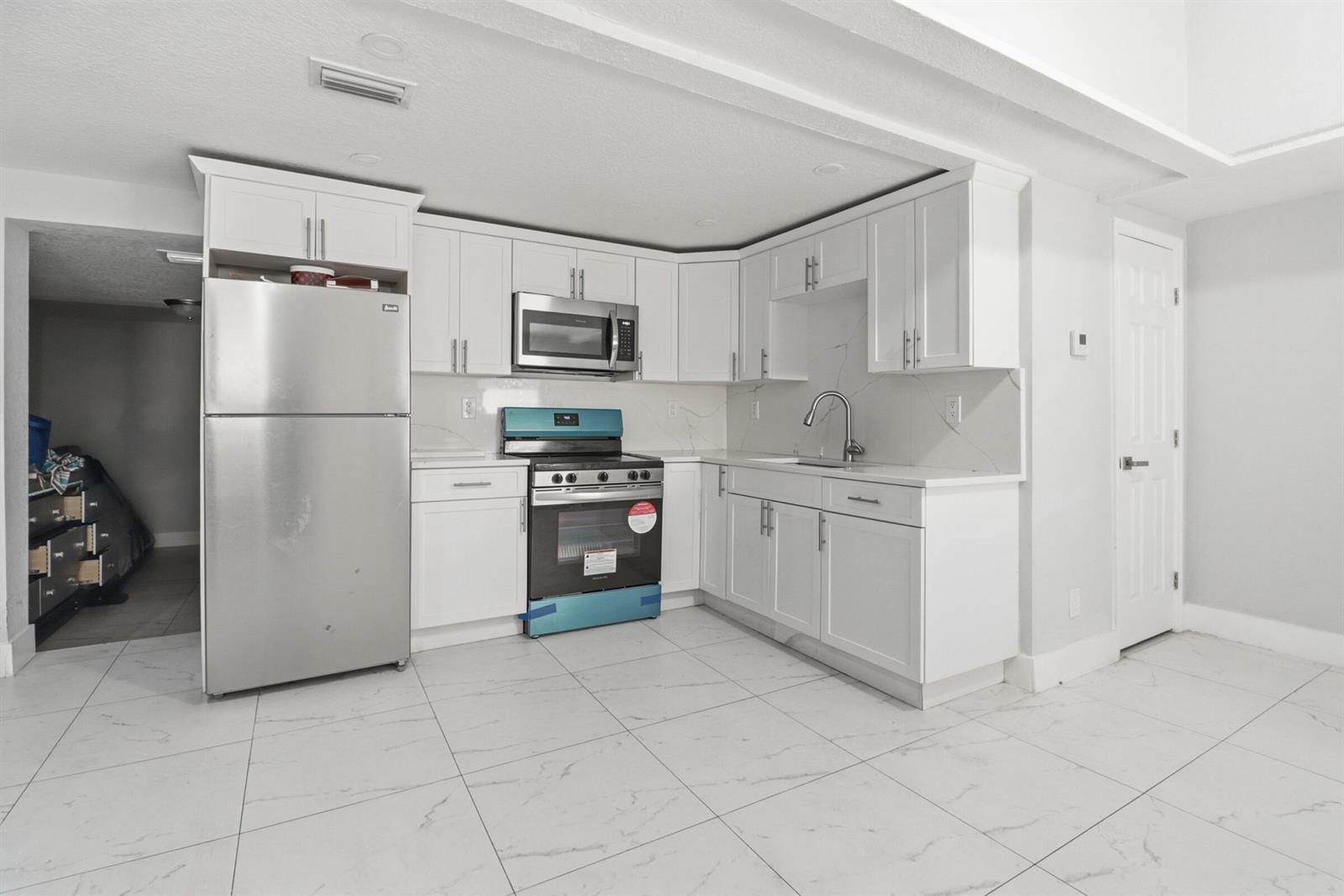 A kitchen features white cabinets, stainless steel appliances, and white marble-patterned tile flooring — 1152 Sunset Road, West Palm Beach FL 33406, WEST PALM BEACH, FL