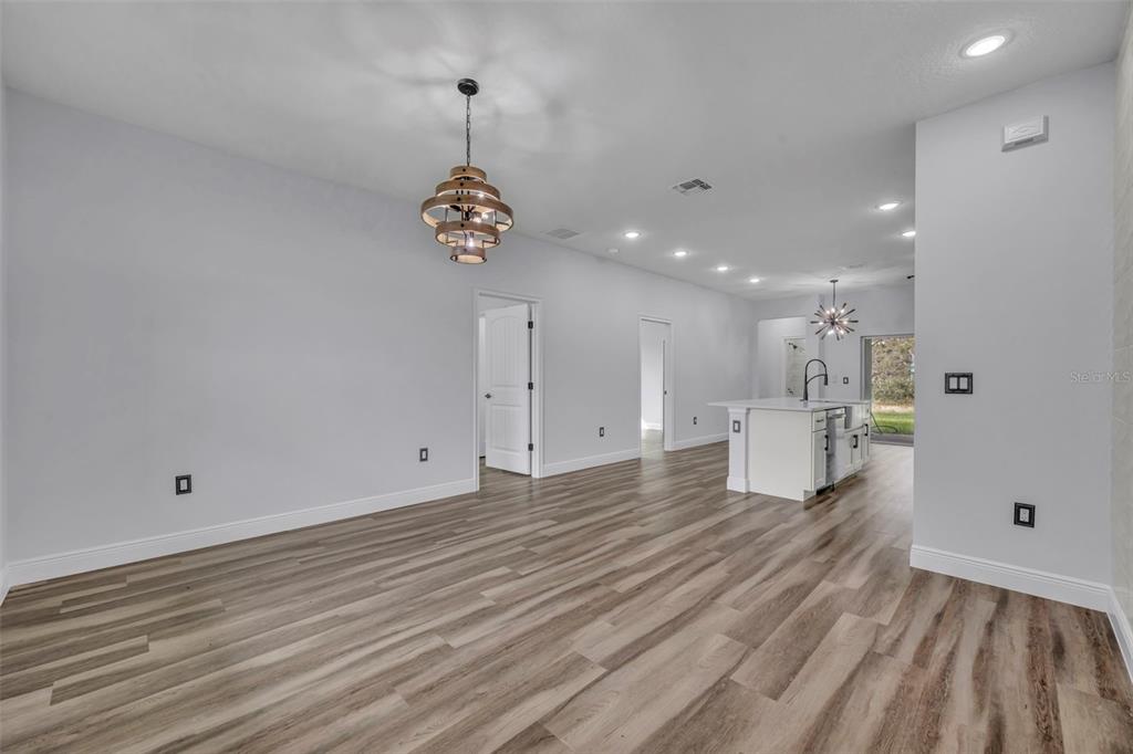 An open-concept living and kitchen area features light gray walls and wood-look plank flooring — 47 ORCHID COURT, POINCIANA, FL