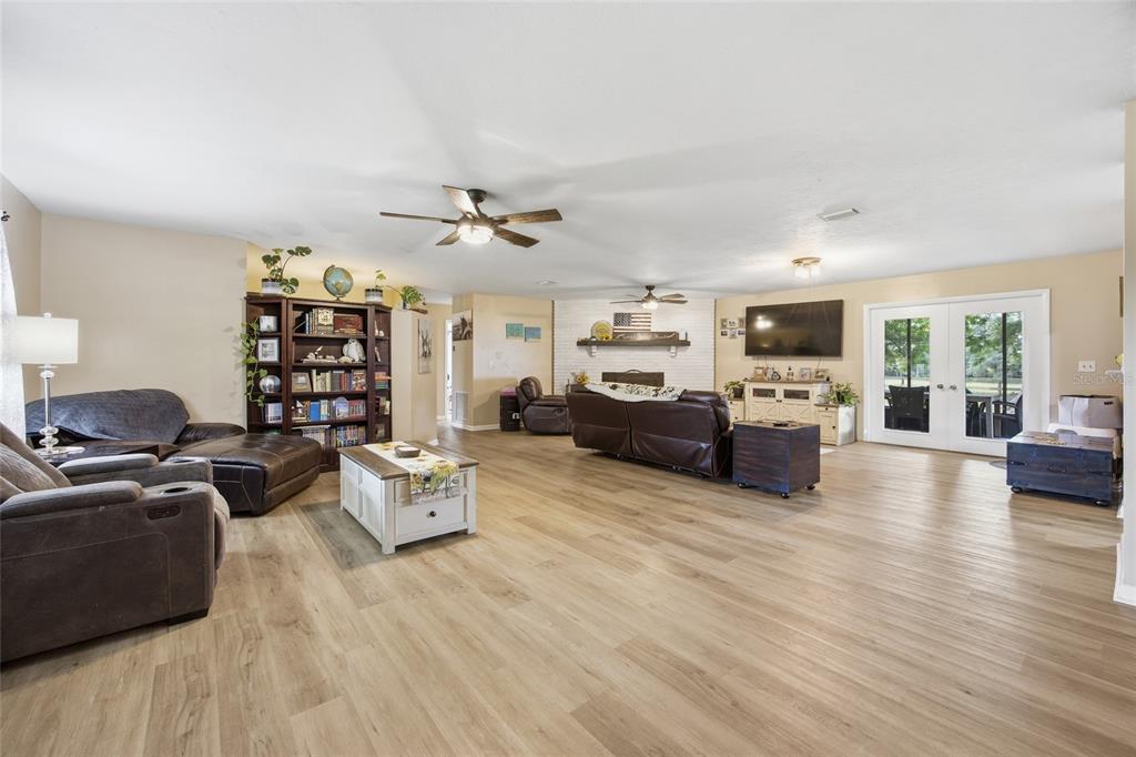 A spacious living room features light wood-look flooring, a brick fireplace, and double glass doors — 13551 NE 14TH AVENUE, CITRA, FL