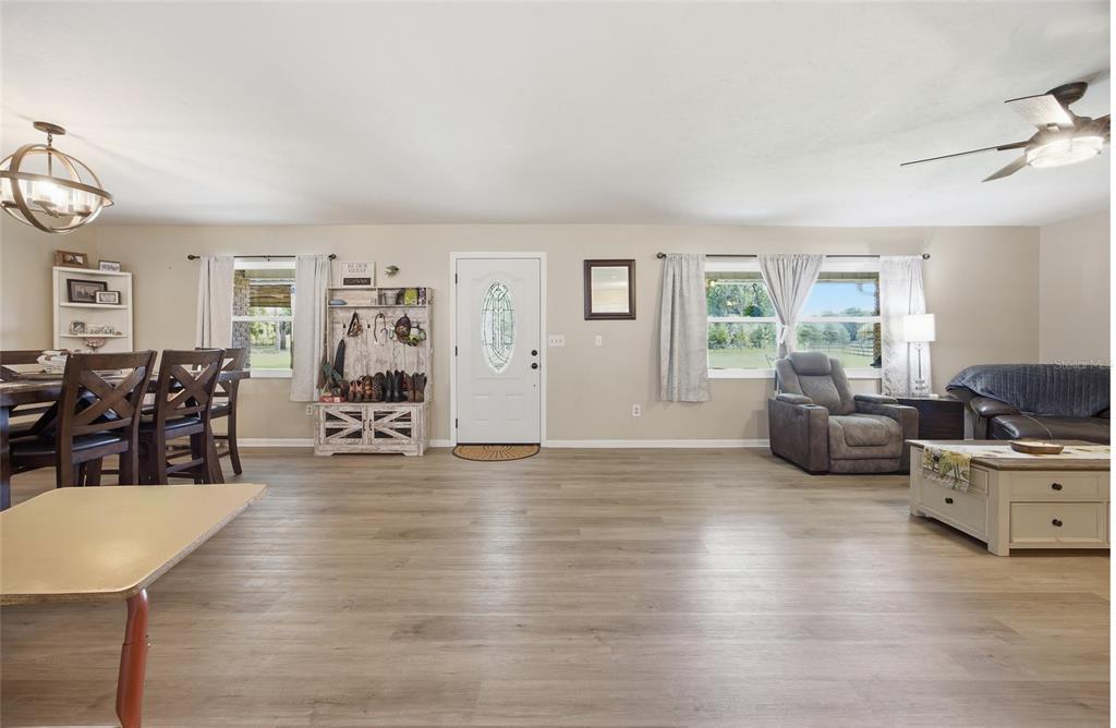 A living and dining area with light wood-look flooring, a front door, and large windows — 13551 NE 14TH AVENUE, CITRA, FL