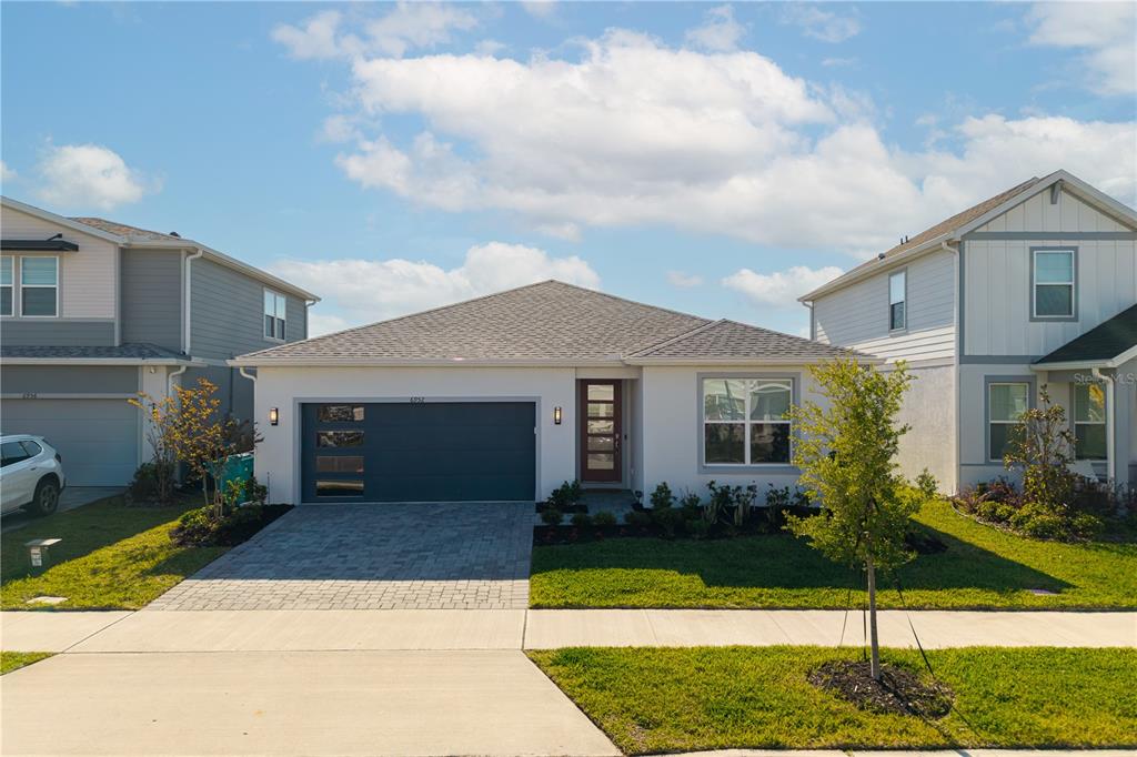 A single-story white house with a gray roof, a dark garage door, and a front lawn — 6952 ROSY SKY AVENUE, ORLANDO, FL