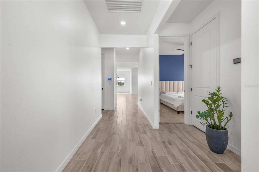 A hallway with light wood-look tile flooring leads toward a bedroom with a blue wall — 6952 ROSY SKY AVENUE, ORLANDO, FL