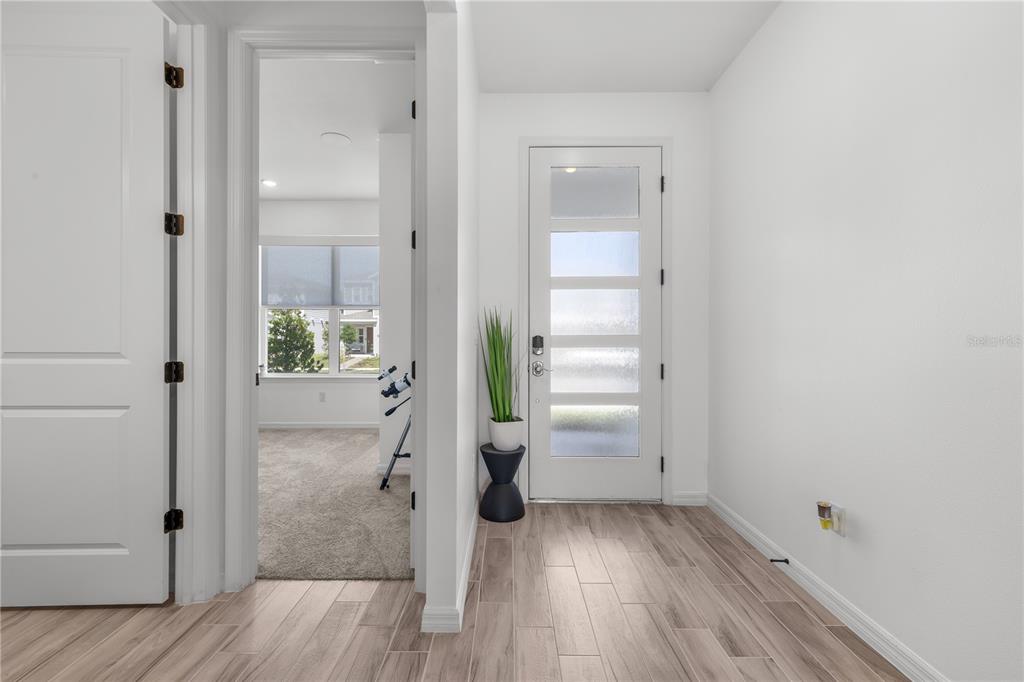 A bright entryway features wood-look tile flooring, a white front door, and a nearby doorway — 6952 ROSY SKY AVENUE, ORLANDO, FL