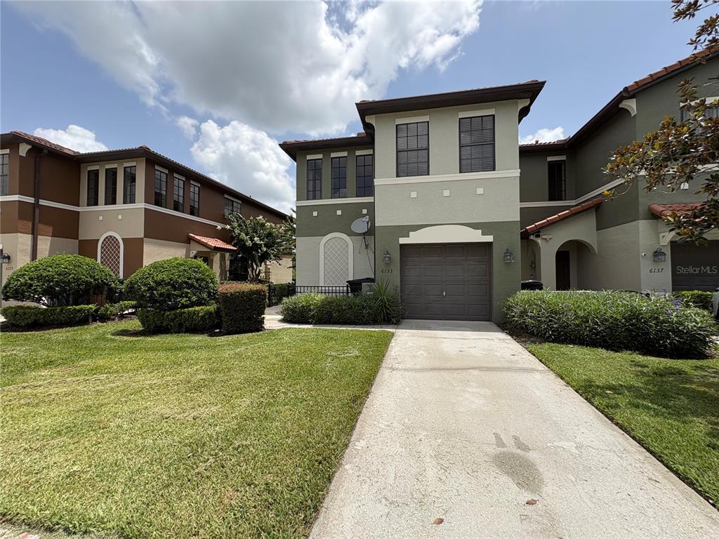 A two-story house with a garage, concrete driveway, and landscaped front yard under a blue sky — 6133 APOLLOS CORNER WAY, ORLANDO, FL