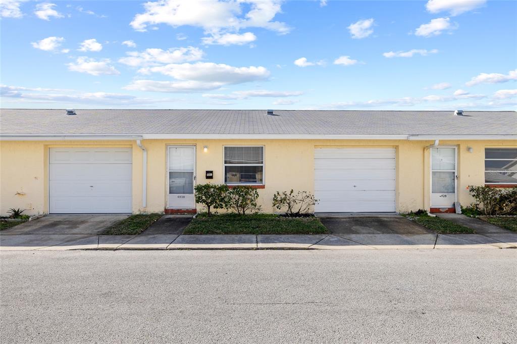A street-level view of two adjacent single-story residential units with garages and yellow stucco walls — 4930 HAZNER STREET, NEW PORT RICHEY, FL