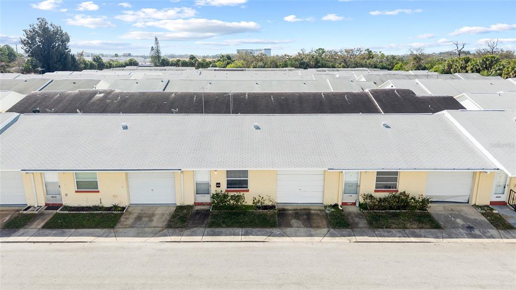 An exterior view of a row of single-story townhomes with light yellow siding and garages — 4930 HAZNER STREET, NEW PORT RICHEY, FL