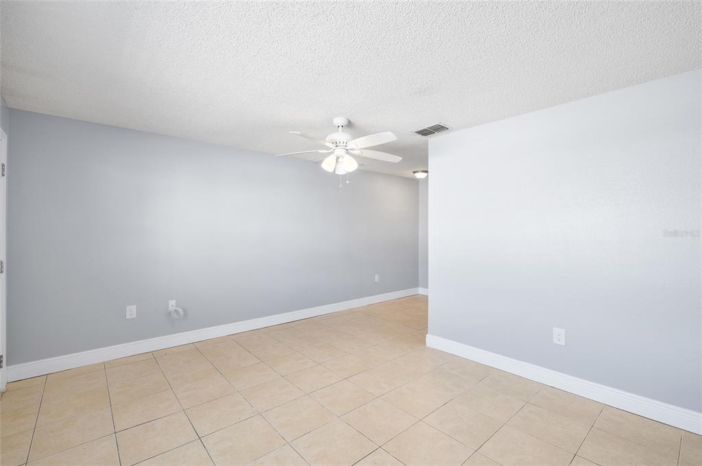 An empty room with light gray walls, white trim, and beige tile flooring — 4930 HAZNER STREET, NEW PORT RICHEY, FL