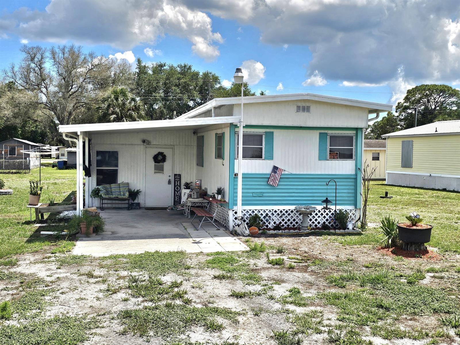 A single-story mobile home with a covered patio, teal accents, and a grassy yard — 17408 Broadwing Lane, Okeechobee FL 34974, OKEECHOBEE, FL
