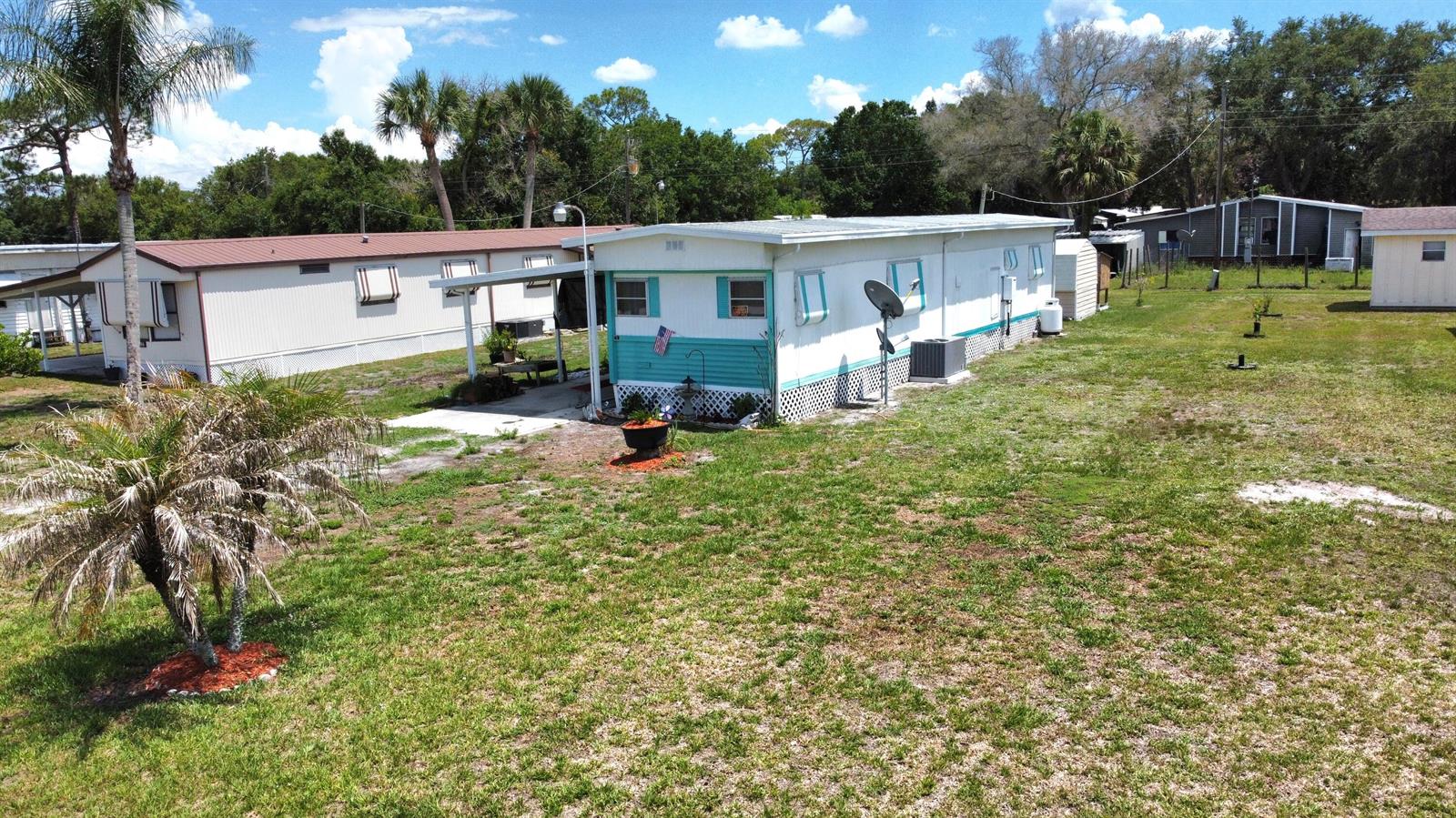 An exterior view of a mobile home with a turquoise accent wall and a yard — 17408 Broadwing Lane, Okeechobee FL 34974, OKEECHOBEE, FL