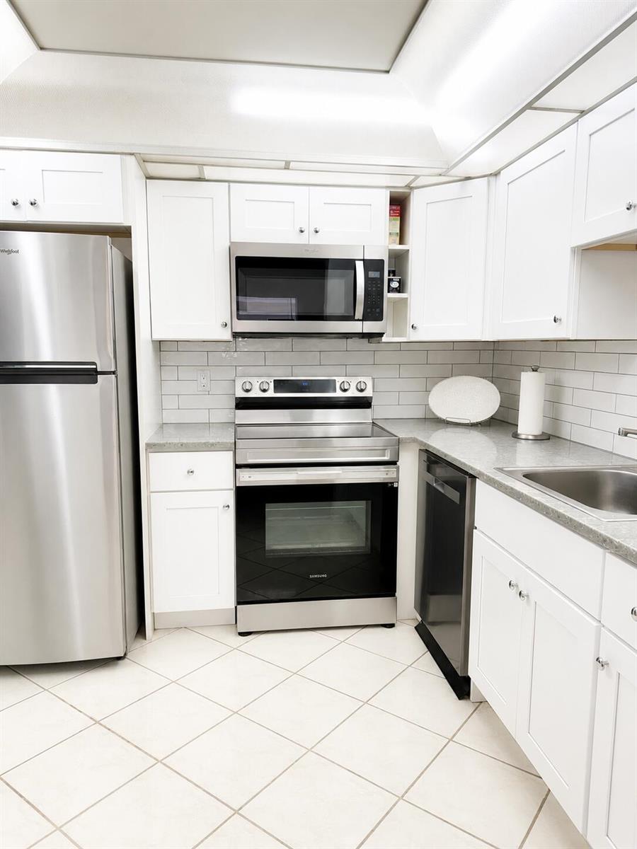 A kitchen features white cabinets, stainless steel appliances, gray countertops, and a white subway tile backsplash — 6 Brittany A # 6a, Delray Beach FL 33446, DELRAY BEACH, FL