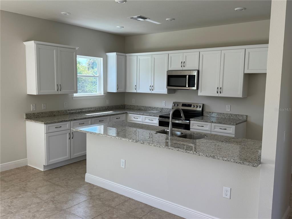 A kitchen features white cabinets, granite countertops, a stainless steel microwave, and a breakfast bar — 3462 SERNICE STREET, NORTH PORT, FL