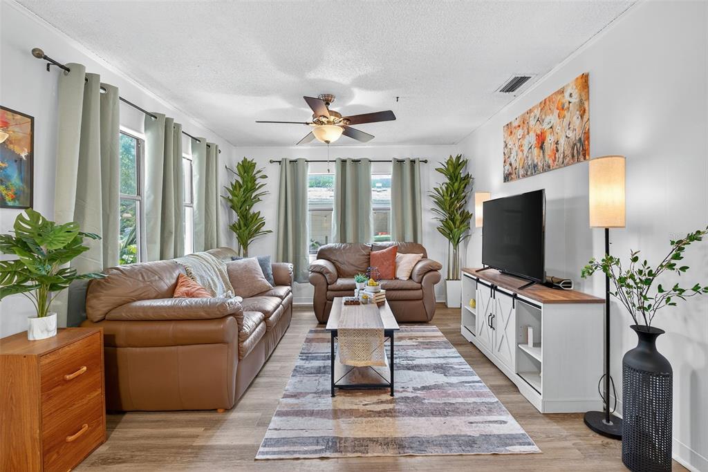 A living room features brown leather sofas, a television on a white console, and curtains — 7009 S FITZGERALD STREET, TAMPA, FL