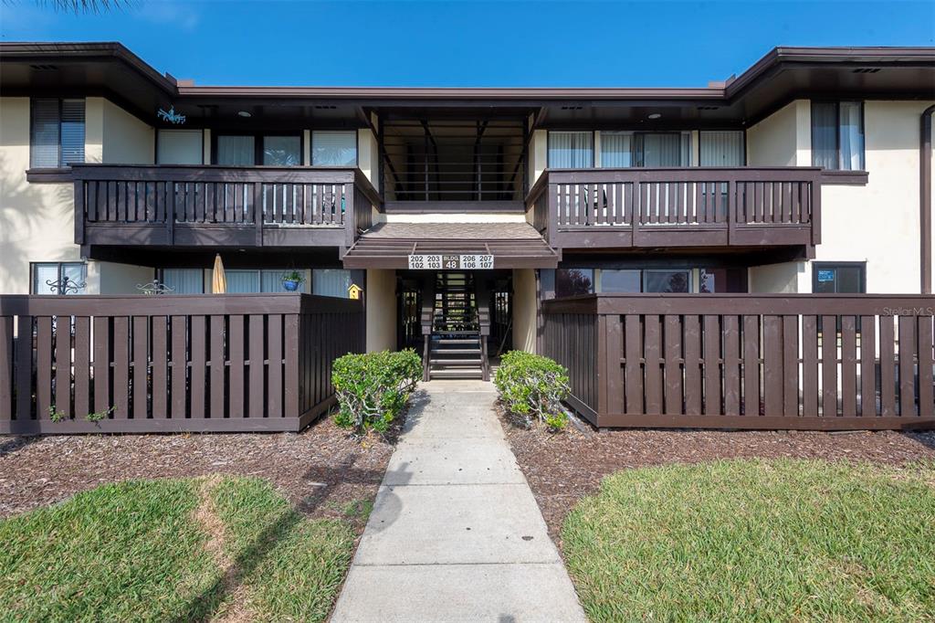 A two-story apartment building exterior features brown wooden balconies and a central staircase — 48 CLUB HOUSE DRIVE UNIT 106, PALM COAST, FL
