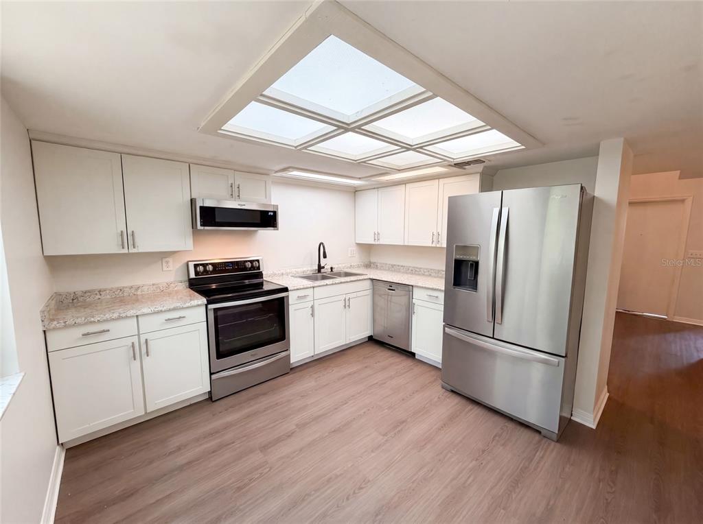 A kitchen features white cabinets, stainless steel appliances, a granite countertop, and a skylight — 830 DUNBAR TERRACE, WINTER SPRINGS, FL