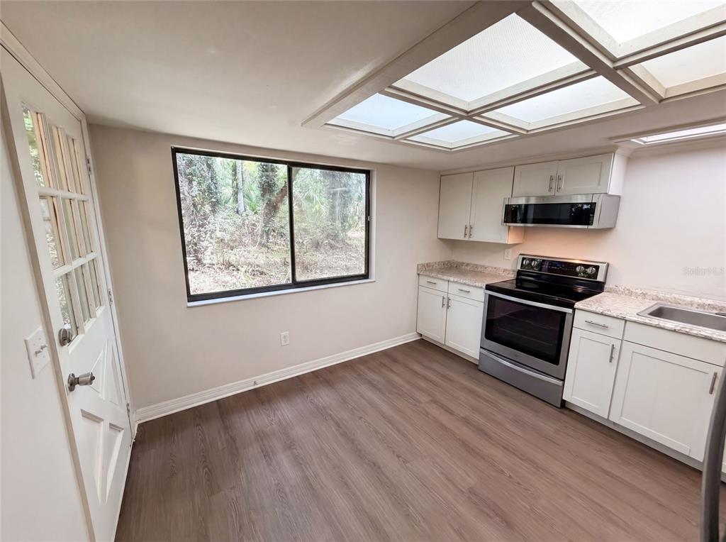 A kitchen with white cabinets, stainless steel appliances, wood-look flooring, and a large skylight — 830 DUNBAR TERRACE, WINTER SPRINGS, FL