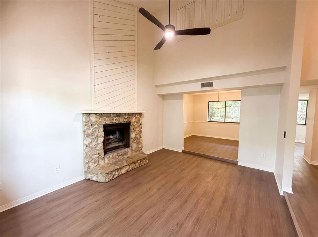 A living room features a stone fireplace, wood-look flooring, and a high ceiling with a fan — 830 DUNBAR TERRACE, WINTER SPRINGS, FL