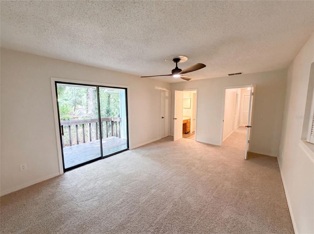 A bedroom with beige carpet, a ceiling fan, and sliding glass doors leading to a deck — 830 DUNBAR TERRACE, WINTER SPRINGS, FL