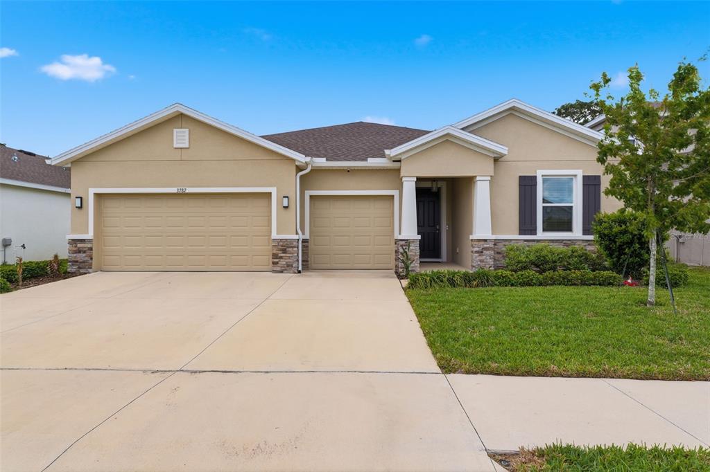A single-story suburban house with a three-car garage, stone accents, and a front porch — 3787 AUTUMN AMBER DRIVE, SPRING HILL, FL