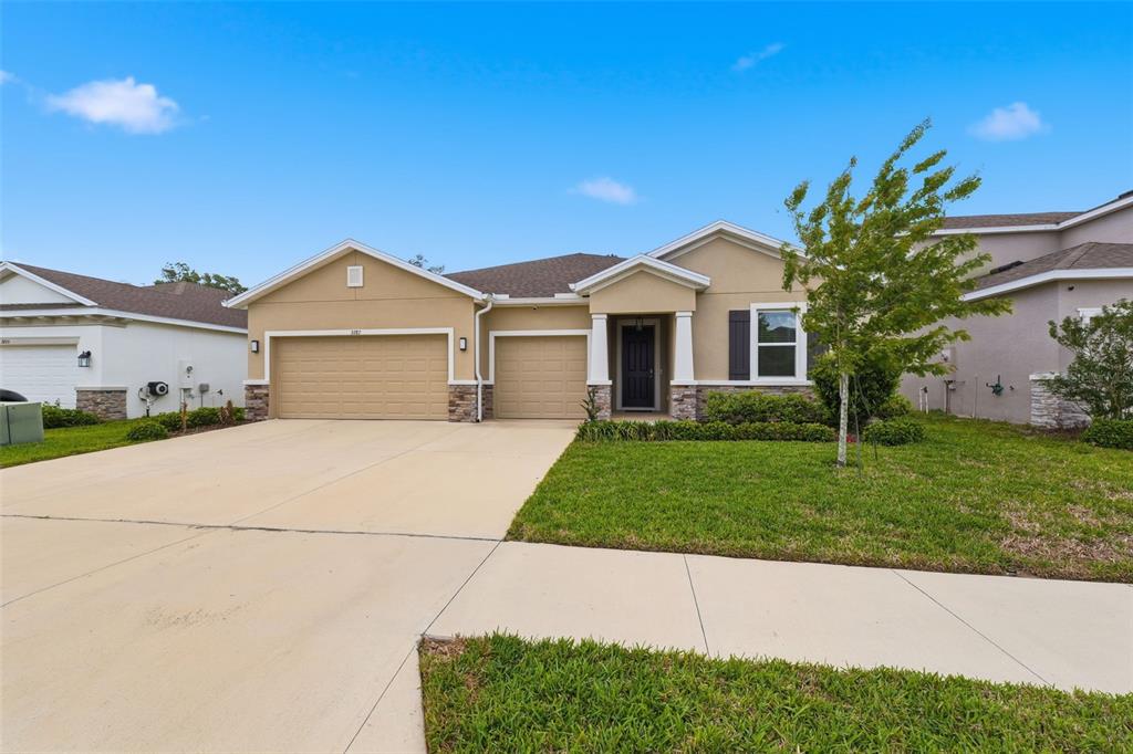 A single-story house with a tan exterior, two-car garage, and a front porch — 3787 AUTUMN AMBER DRIVE, SPRING HILL, FL