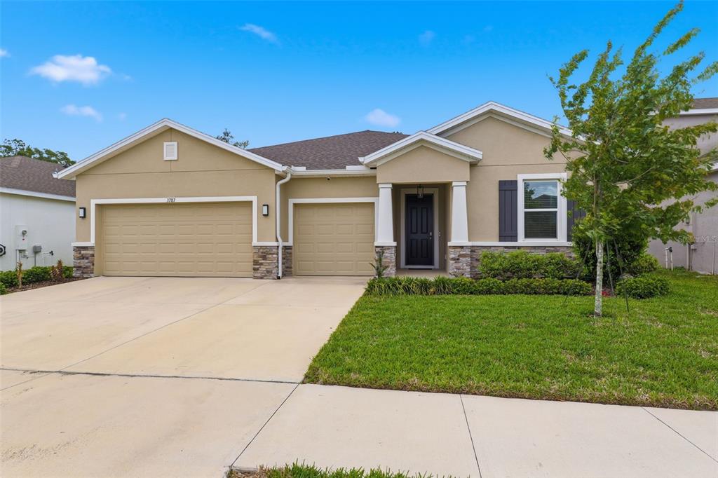 A single-story house with a tan stucco exterior, stone accents, and a three-car garage — 3787 AUTUMN AMBER DRIVE, SPRING HILL, FL