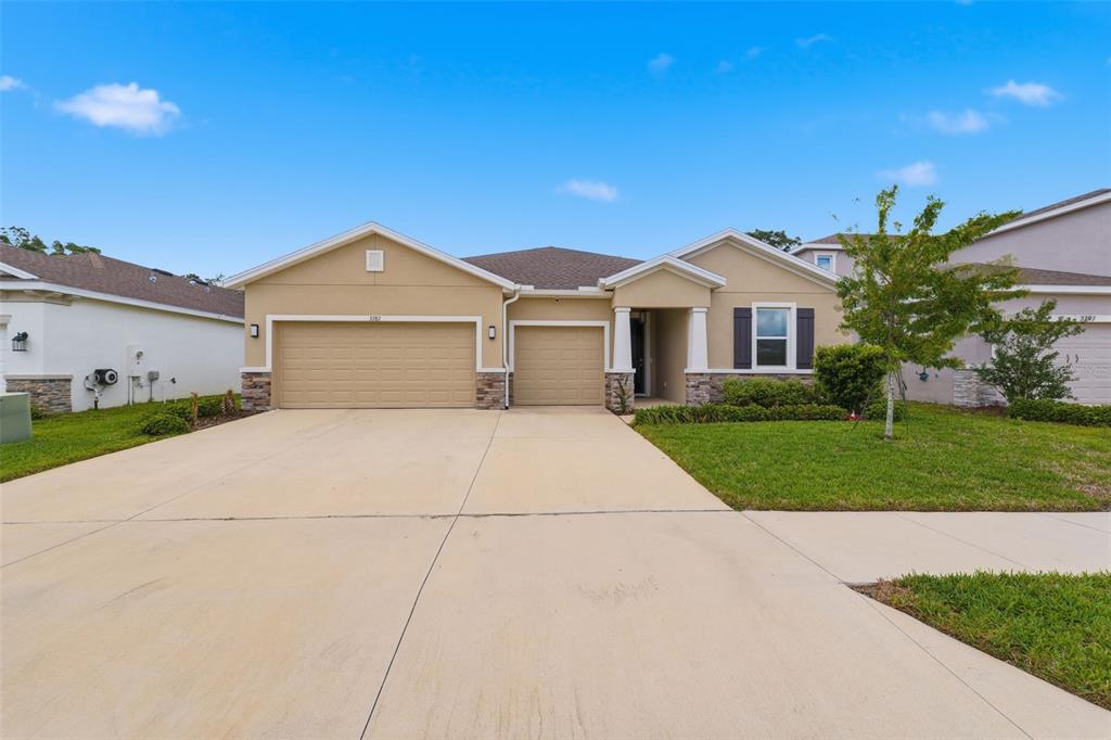 A tan single-story house with a three-car garage, stone accents, and a concrete driveway — 3787 AUTUMN AMBER DRIVE, SPRING HILL, FL