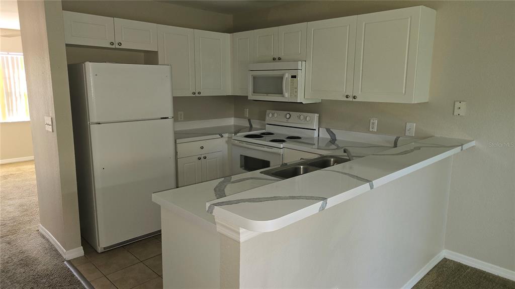 A kitchen with white cabinets, white appliances, and a white countertop with grey veining — 336 CERVANTES DRIVE UNIT 336, KISSIMMEE, FL