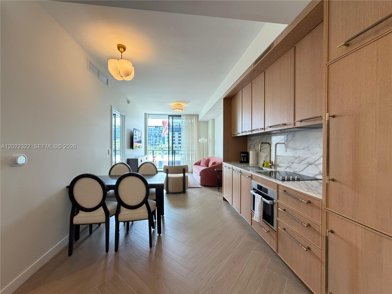 A modern kitchen and dining area features light wood cabinetry, herringbone flooring, and balcony access — 2700 NW 2nd Ave # 305, Miami FL 33127, MIAMI, FL